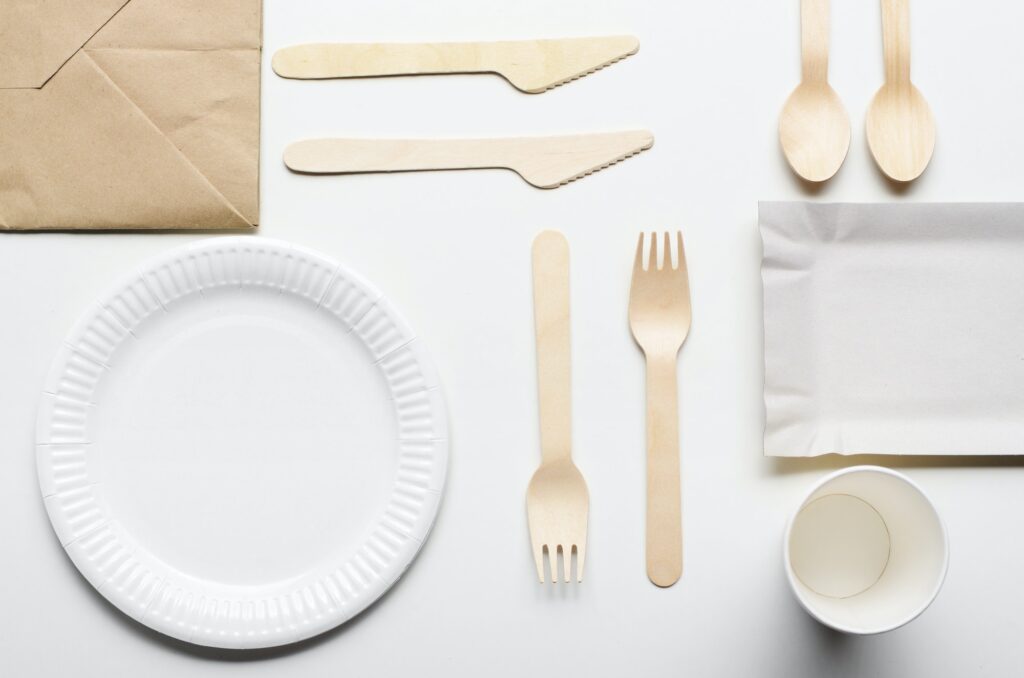 Wooden single use kitchenware and paper shopping bag on white. T